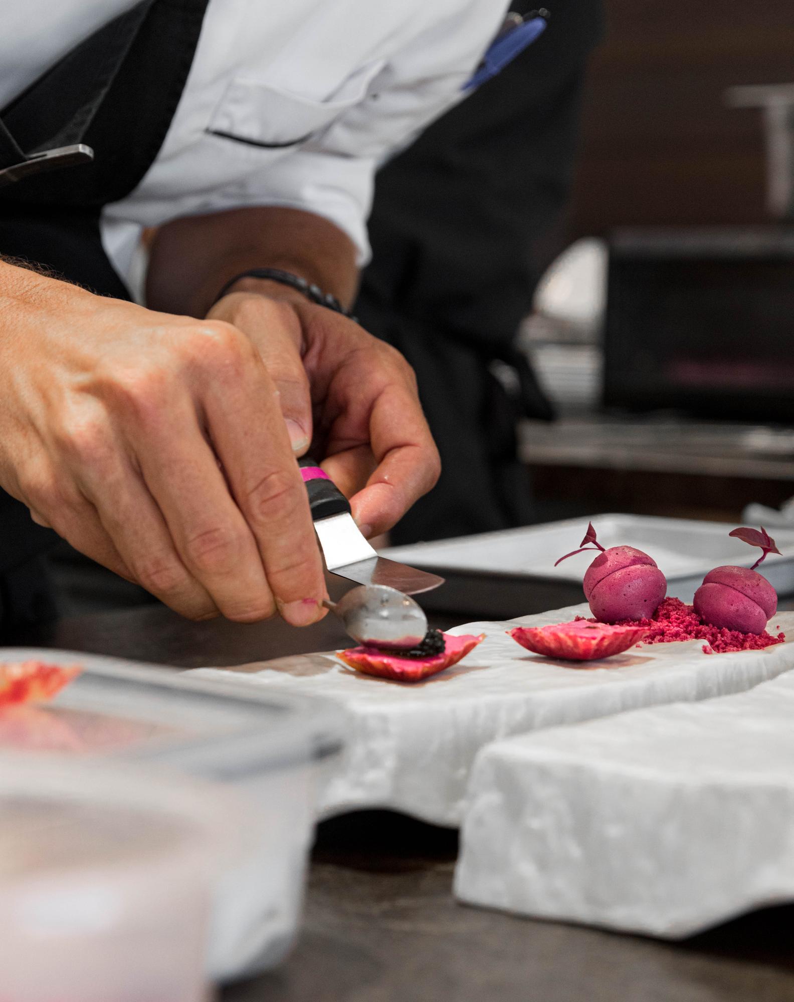 chef la lucru într-o bucătărie deschisă, pregătind garnituri